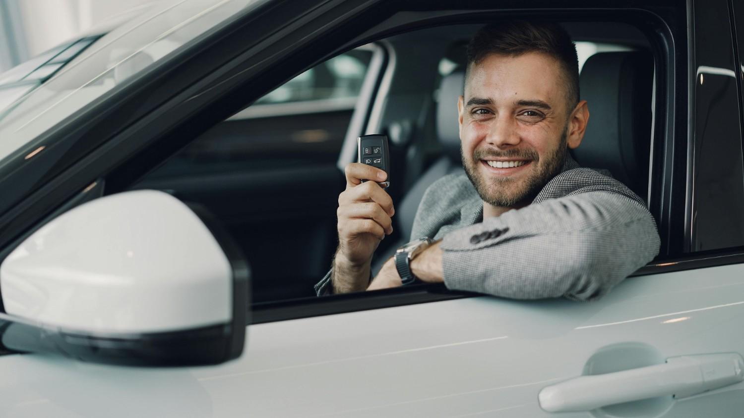 A smiling person holding car keys in front of a new vehicle representing savings